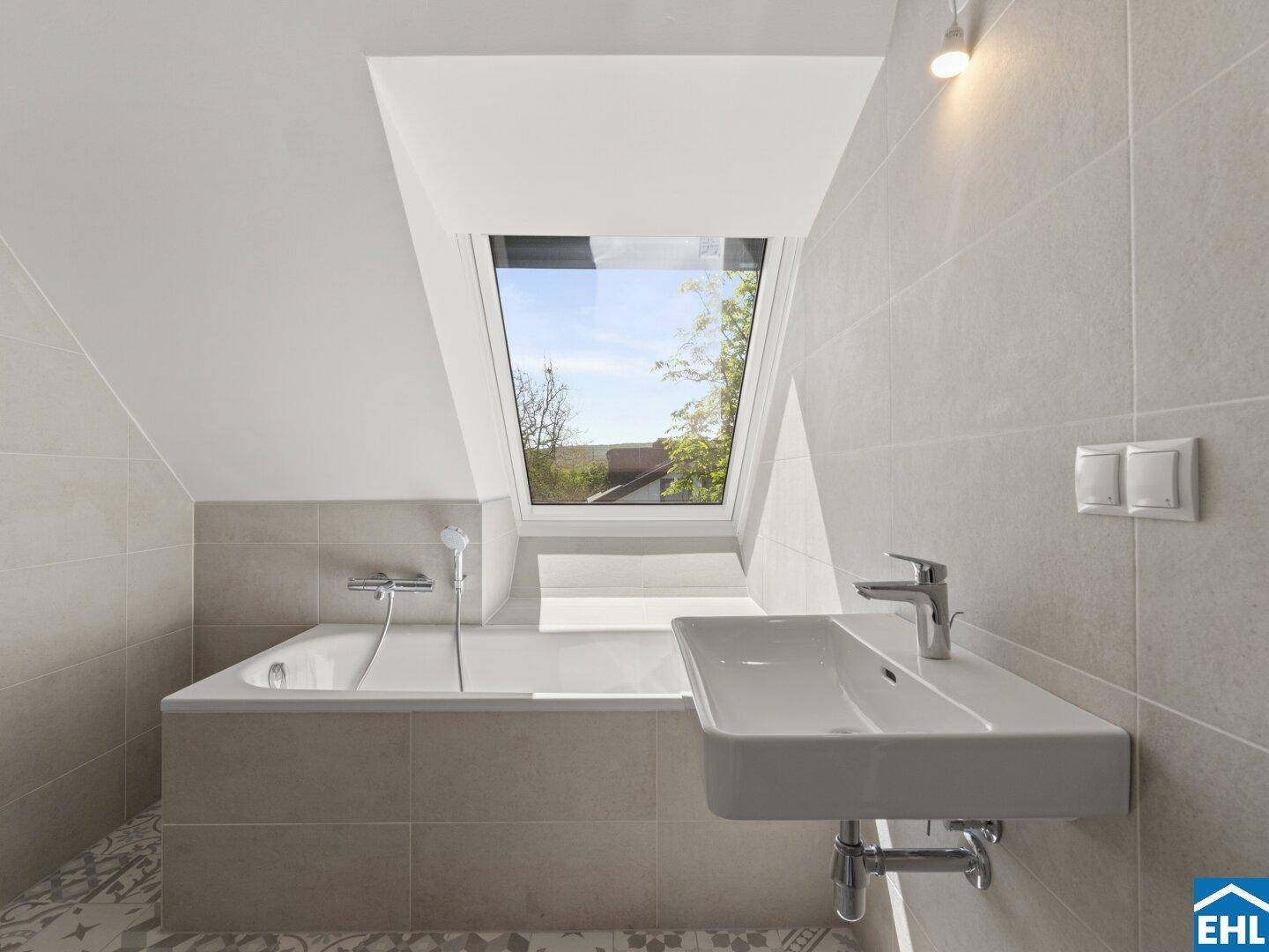 Modernes Badezimmer im Dachgeschoss mit Badewanne, Waschbecken und Dachfenster.