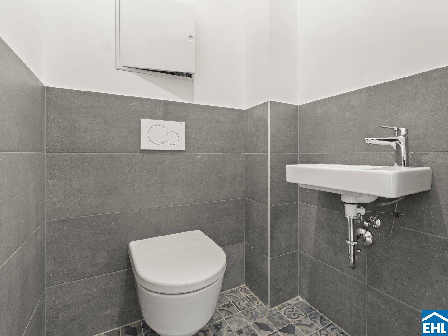 Kleines Gäste-WC mit modernen grauen Fliesen, wandhängender Toilette und Waschbecken.