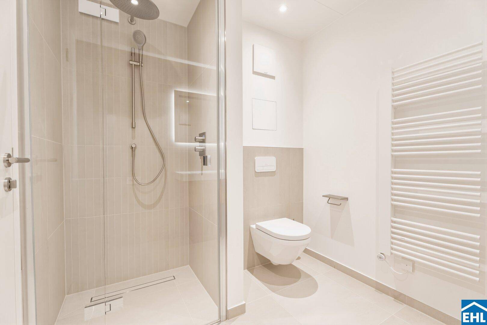 Modernes Badezimmer mit ebenerdiger Dusche, wandhängendem WC und beheiztem Handtuchhalter in hellen Farbtönen.
