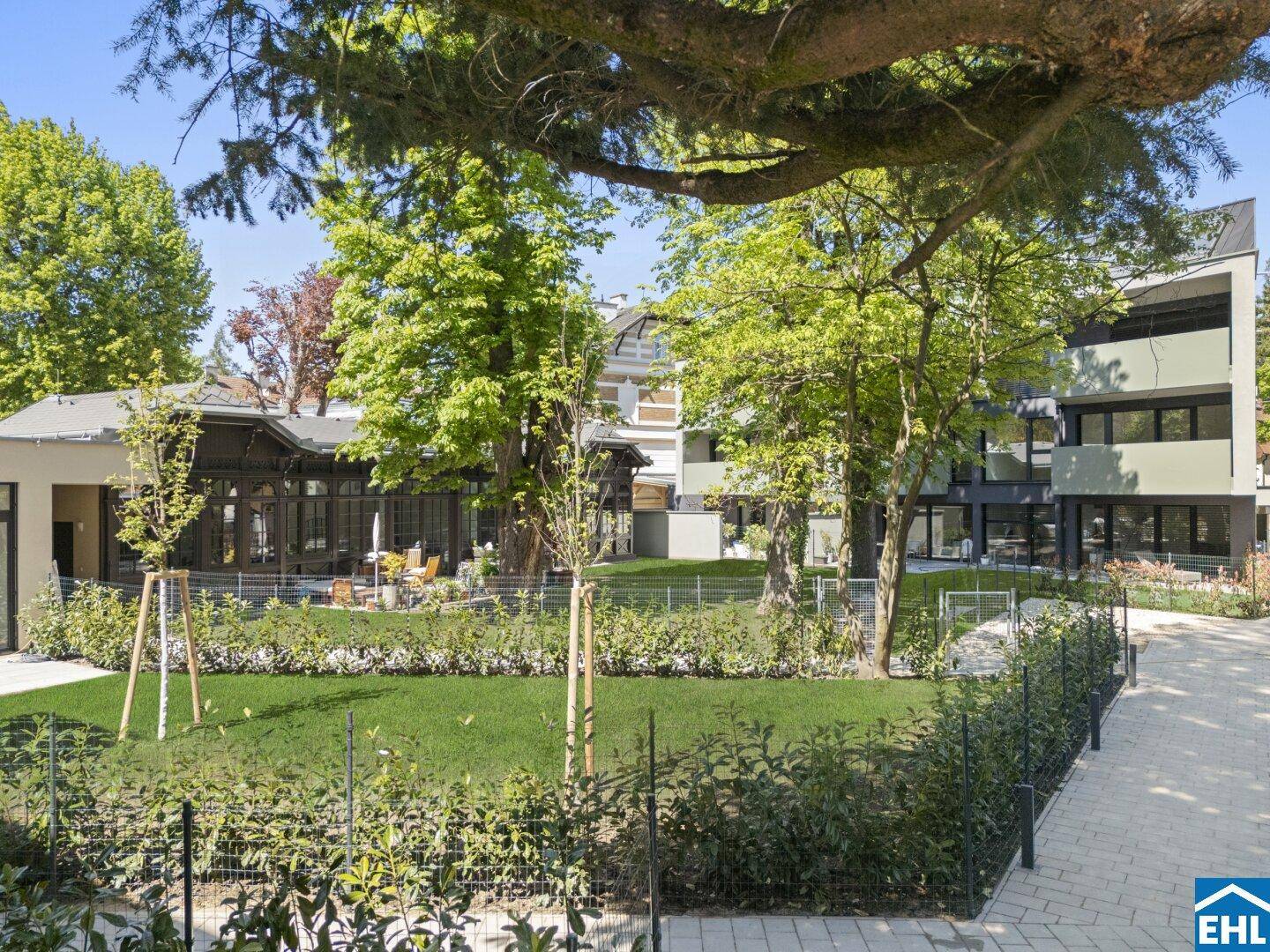 Moderner Gebäudekomplex mit gepflegtem Gartenbereich und einladender Außenterrasse unter Bäumen.