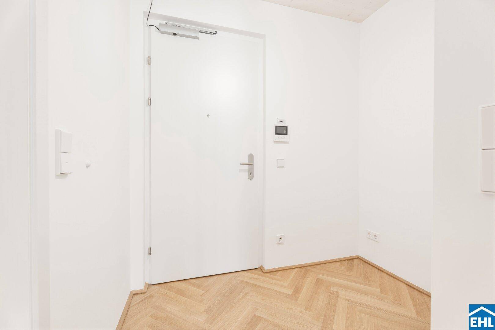Heller Eingangsbereich mit Fischgrätparkett und moderner Wohnungstür.