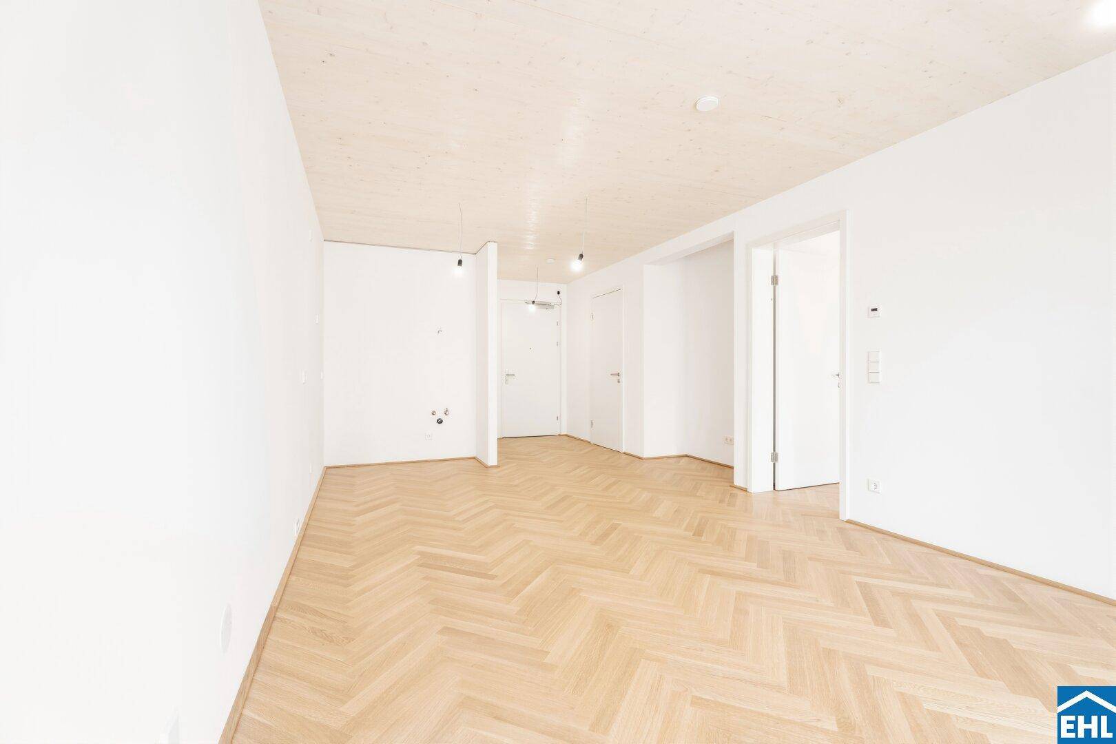 Großzügiger, heller Raum mit elegantem Fischgrätparkett und Holzakzenten an der Decke.