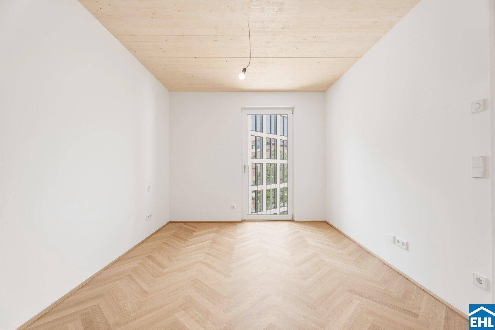 Helles Schlafzimmer mit Fischgrätparkett und einer Tür zu einem französischen Balkon.