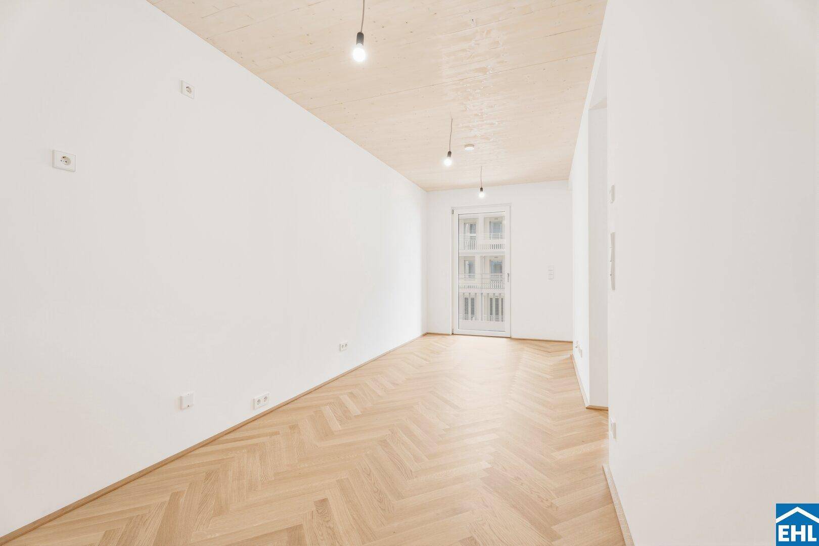 Lichtdurchfluteter Raum mit Fischgrätparkett und einer Tür, die viel Tageslicht hereinlässt.