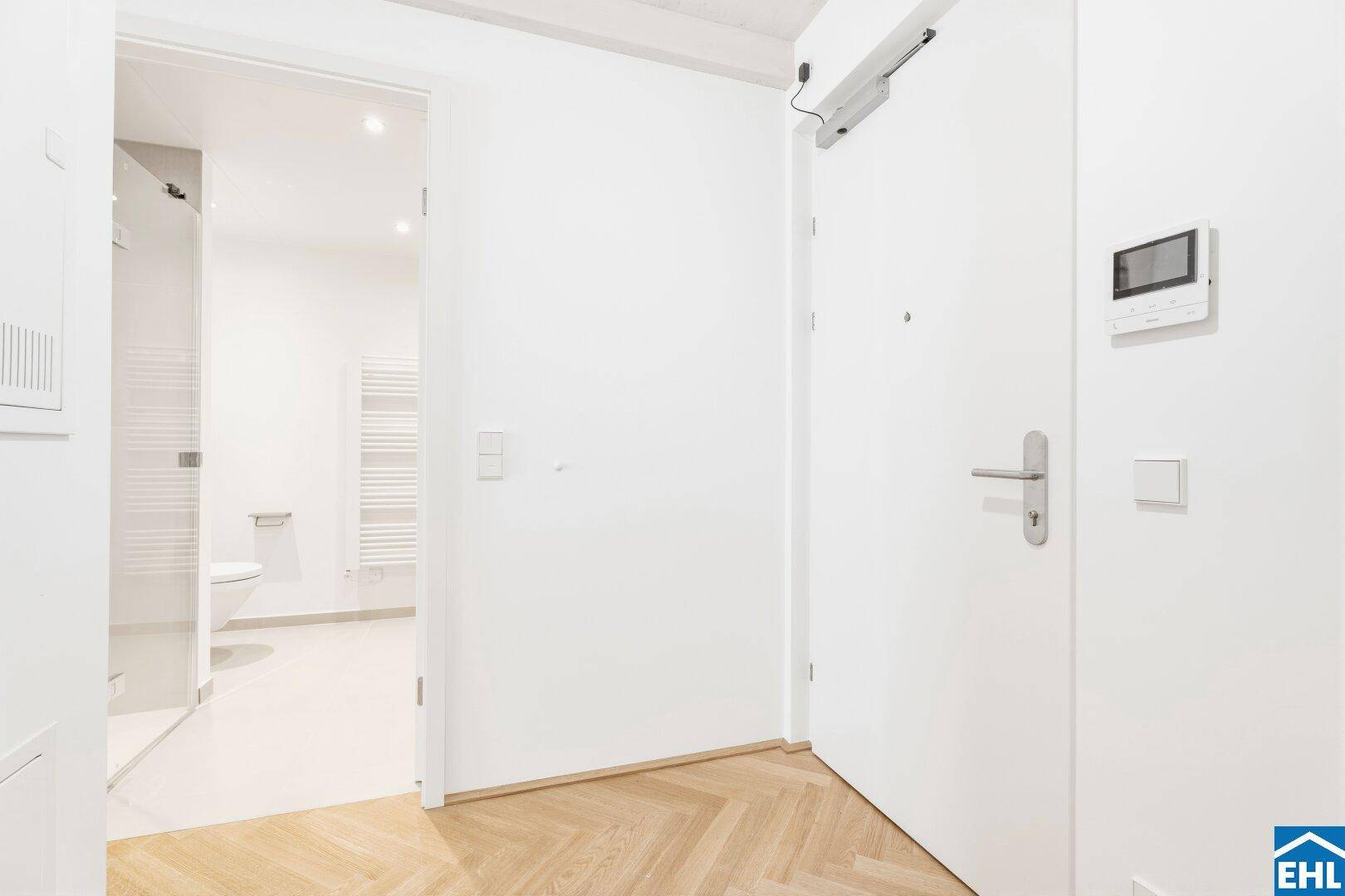Eingangsbereich mit Fischgrätparkett und Blick in das moderne Badezimmer.