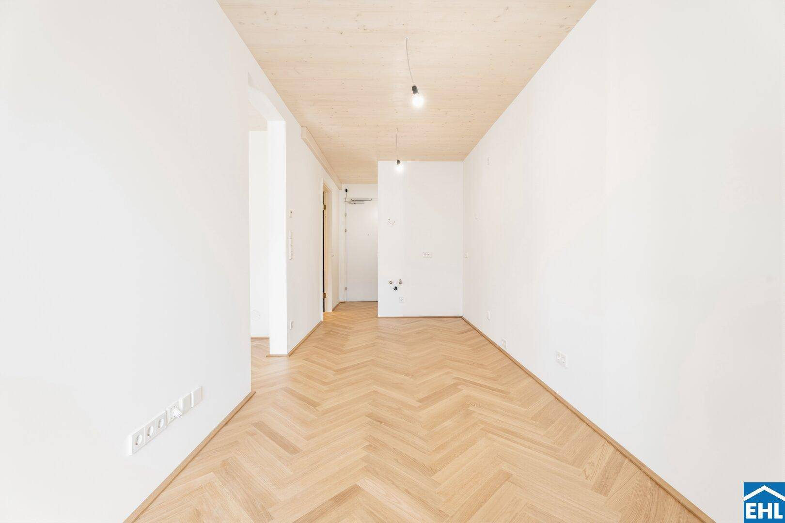 Lichtdurchfluteter Raum mit hellem Fischgrätparkett und einer Decke aus hellem Holz.