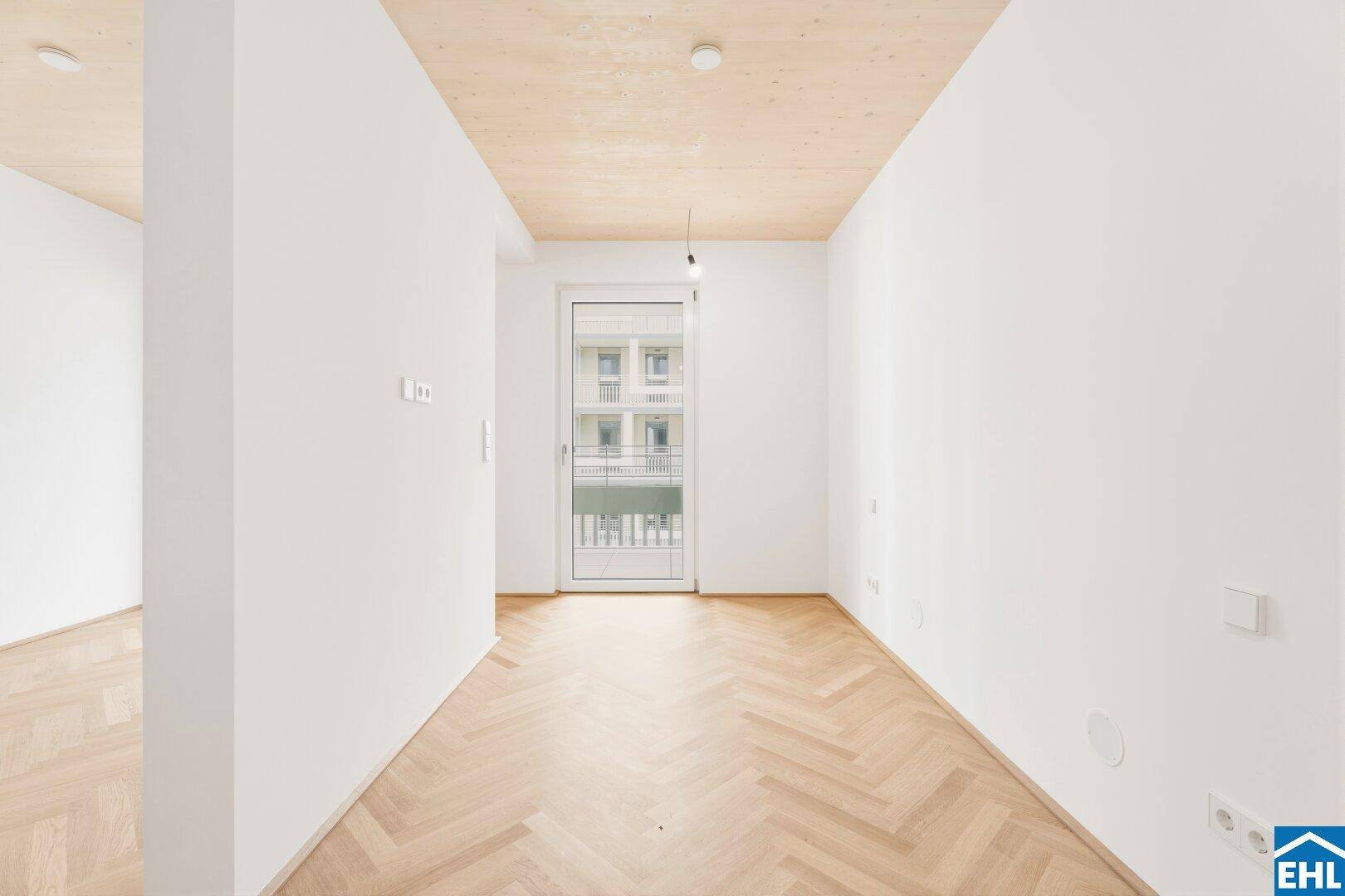 Geräumiges, leeres Zimmer mit Fischgrätparkett und einem französischen Balkon.