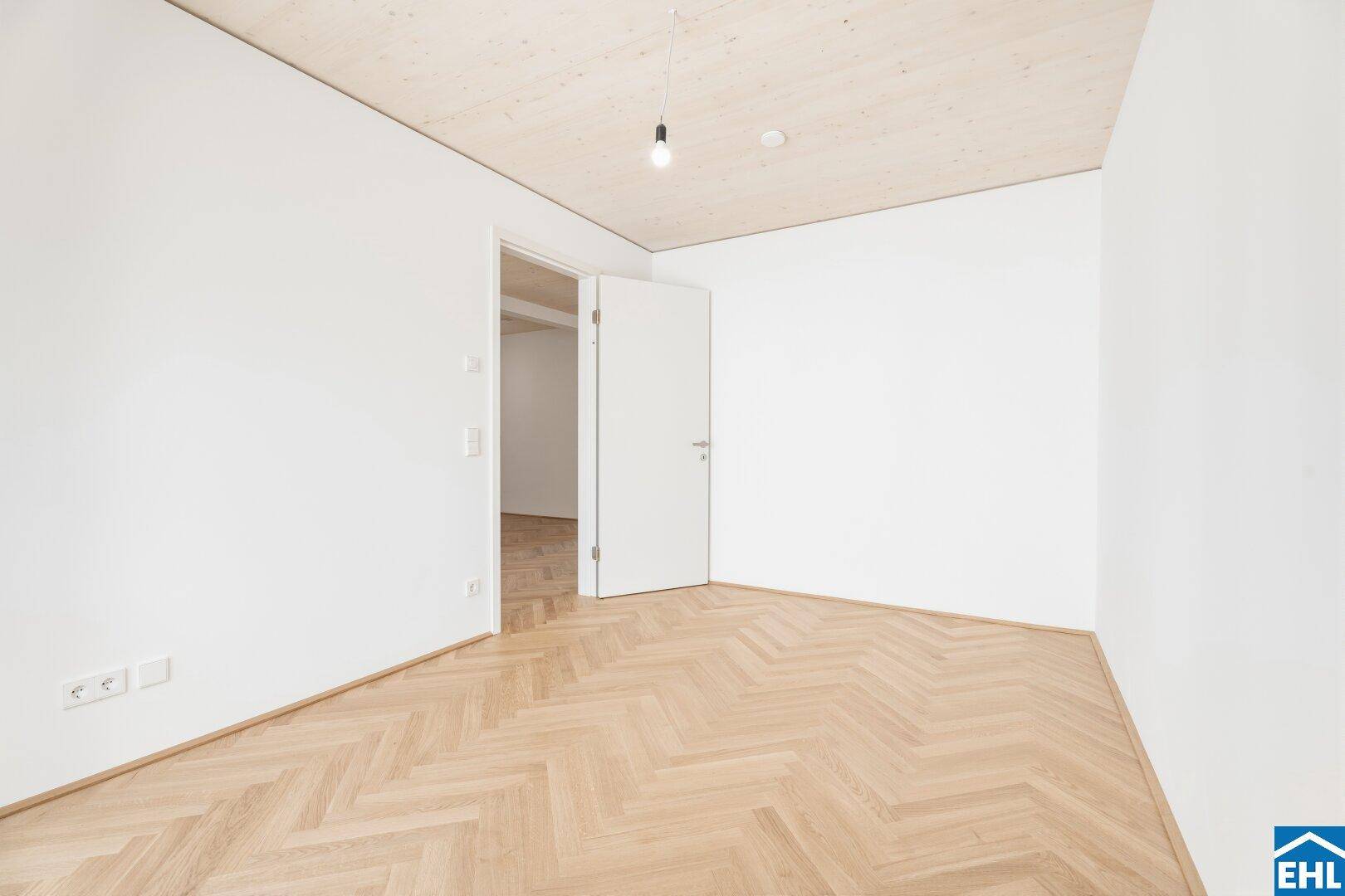 Leeres Schlafzimmer mit Fischgrätparkett und Zugang zu einem weiteren Raum.
