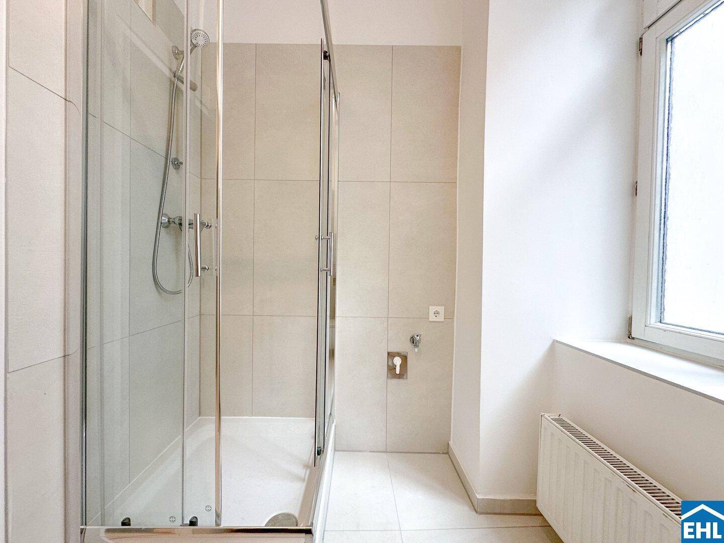 Modernes Badezimmer mit Duschkabine aus Glas, hellen Fliesen und Fenster.
