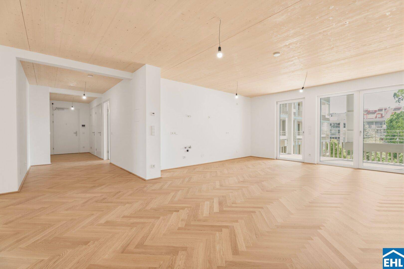 Offener Wohnbereich mit Fischgrätparkett, Holzdecke und Zugang zu einem französischen Balkon.