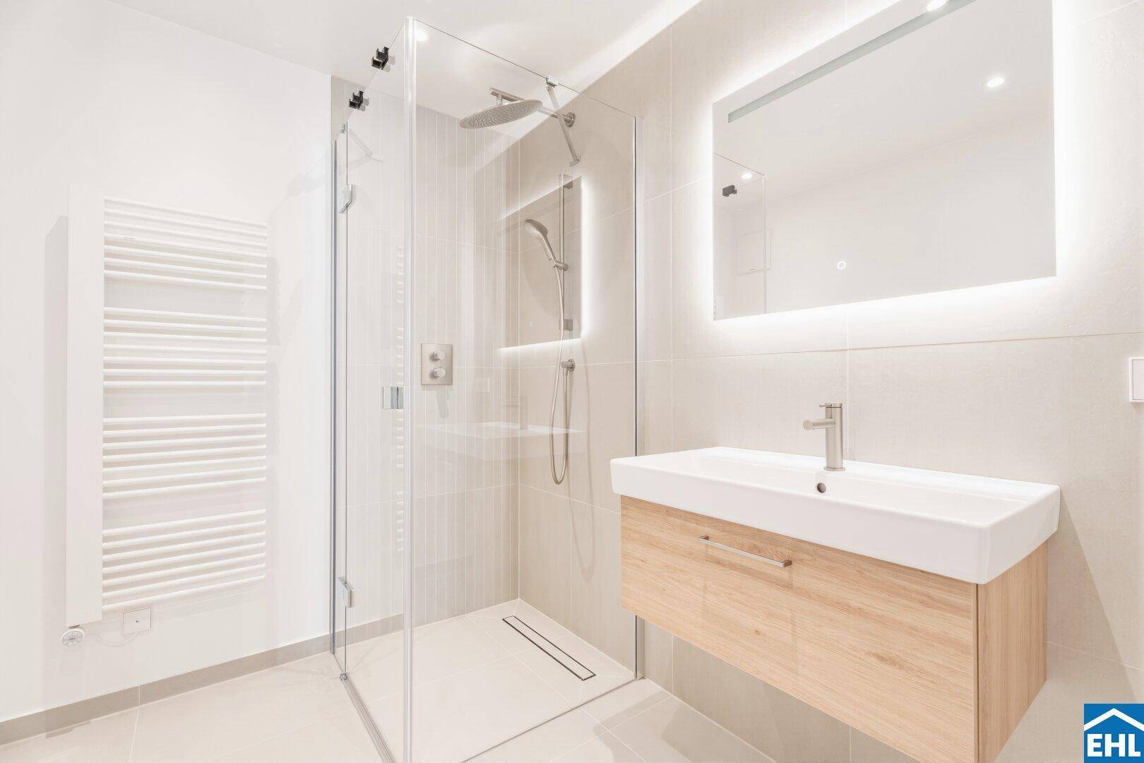 Modernes Badezimmer mit begehbarer Dusche, Holzwaschtisch und beleuchtetem Spiegel.