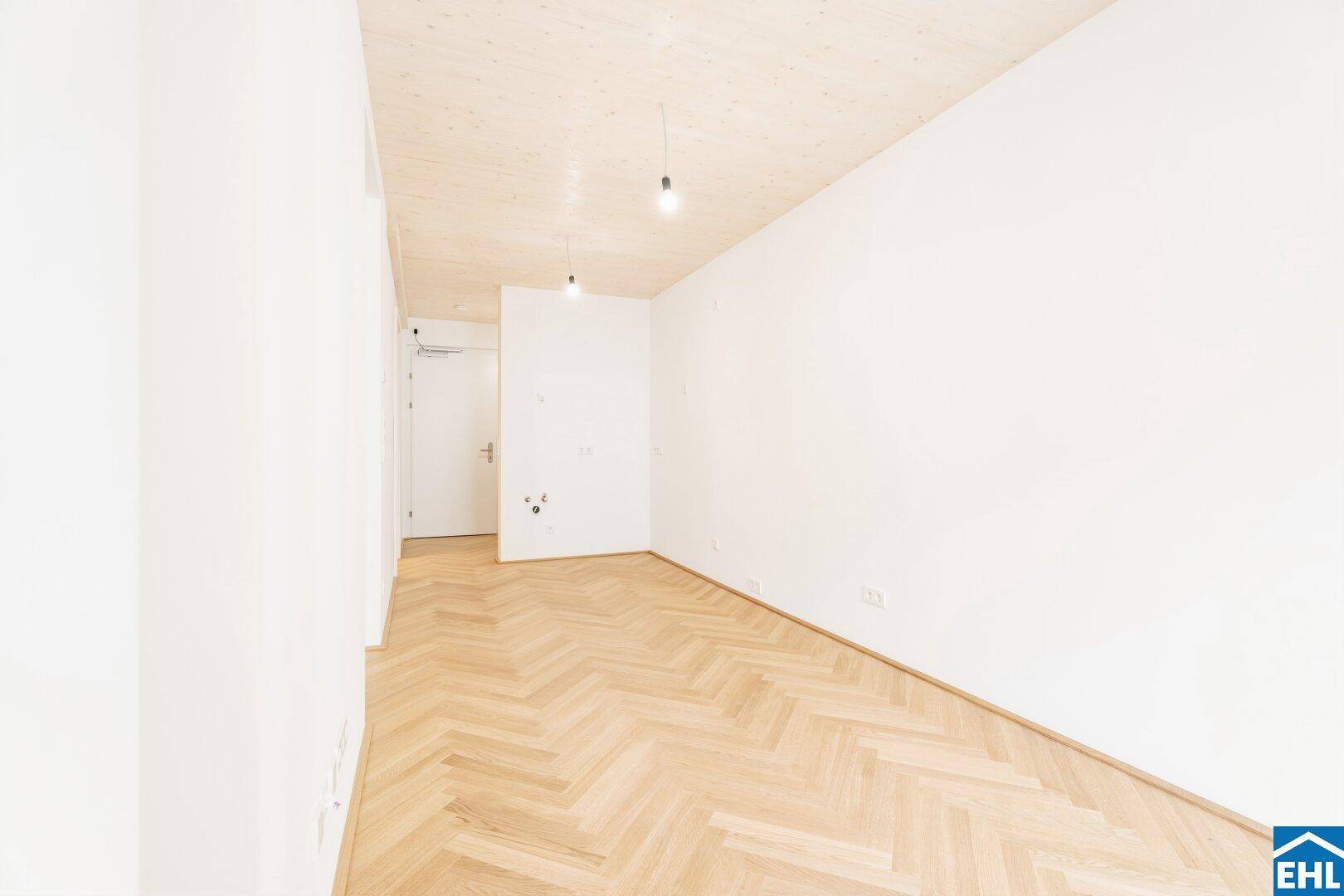 Geräumiges, unmöbliertes Zimmer mit hellem Fischgrätparkett und Holzbalkendecke, bereit zur Gestaltung.