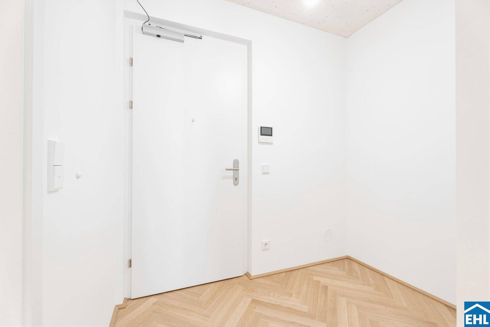 Heller Eingangsbereich mit moderner weißer Tür und Fischgrätparkettboden, einladend und funktional.