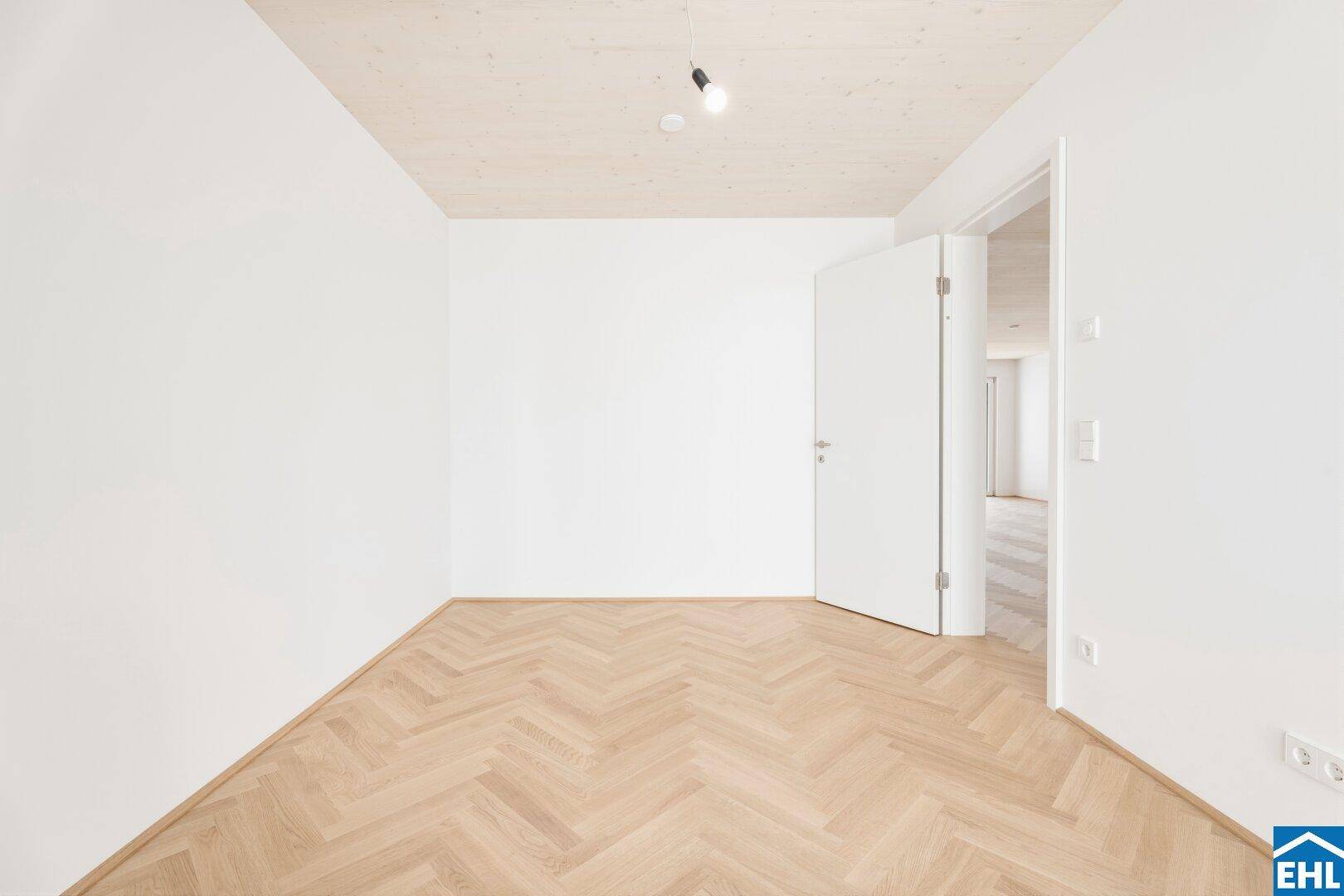 Geräumiges Schlafzimmer mit Fischgrätparkett, Holzbalkendecke und weiß gestrichenen Wänden.