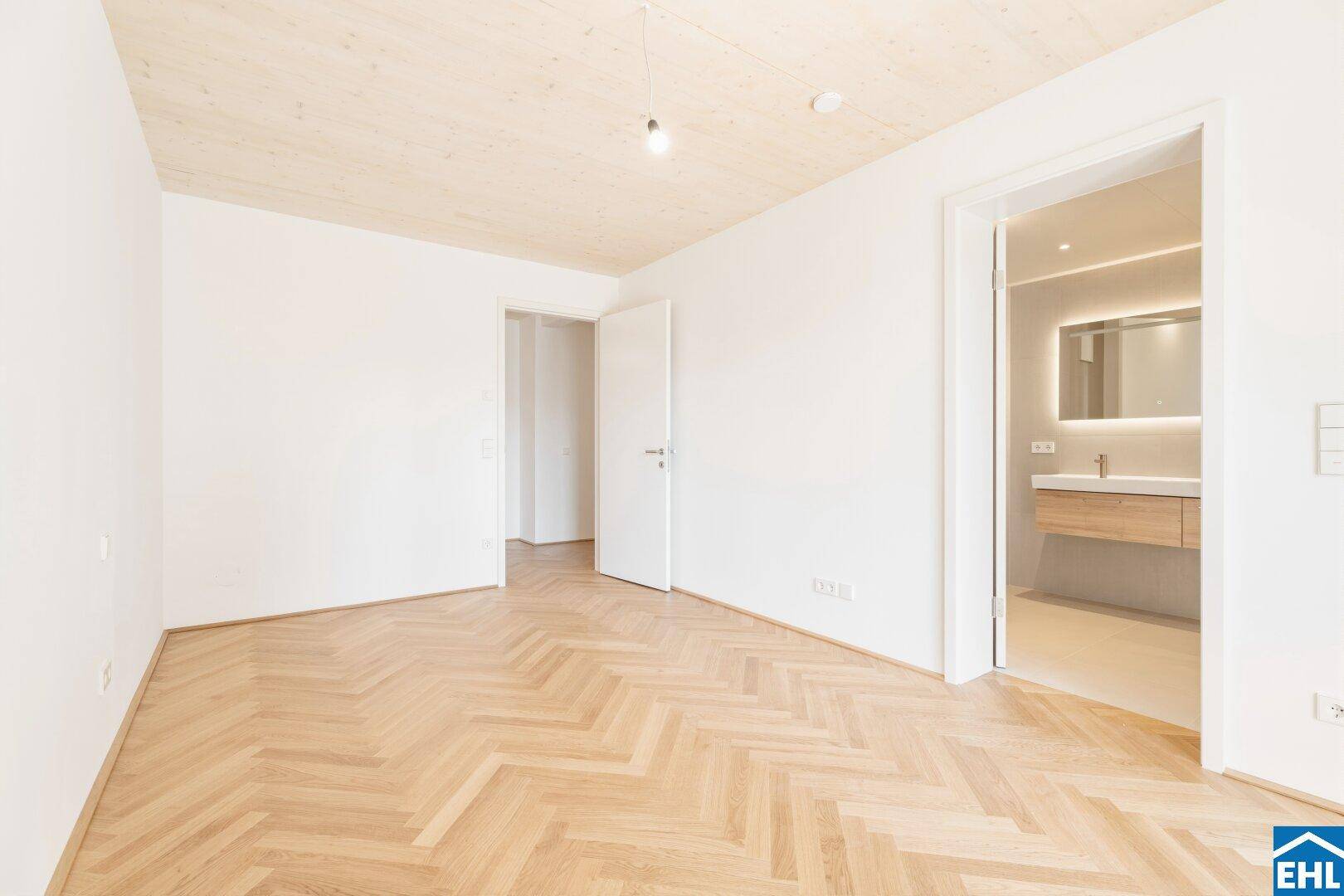 Schlafzimmer mit Fischgrätparkett und direktem Zugang zu einem modernen Badezimmer.