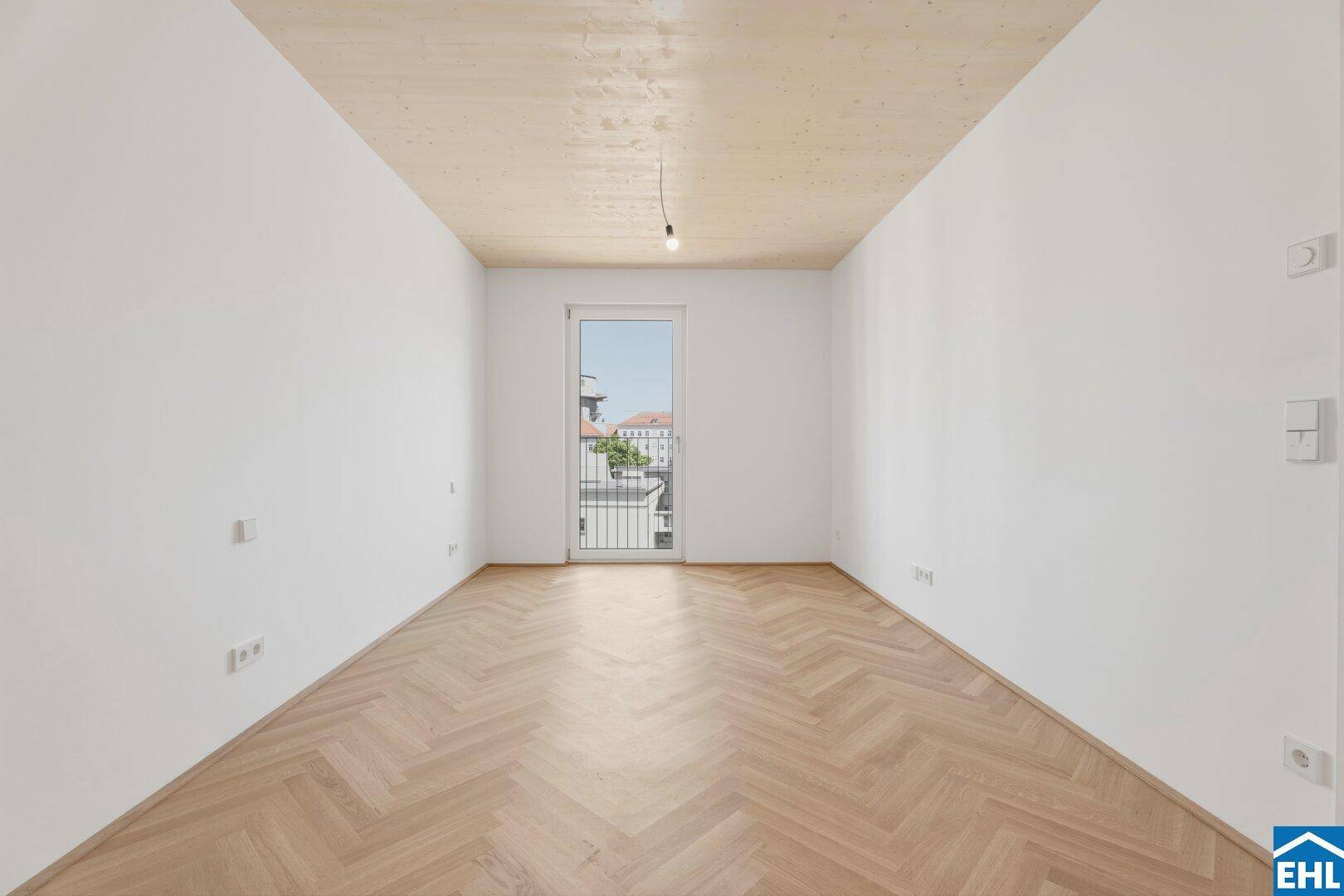 Helles Zimmer mit Fischgrätparkett, Holzbalkendecke und einem französischen Balkon.