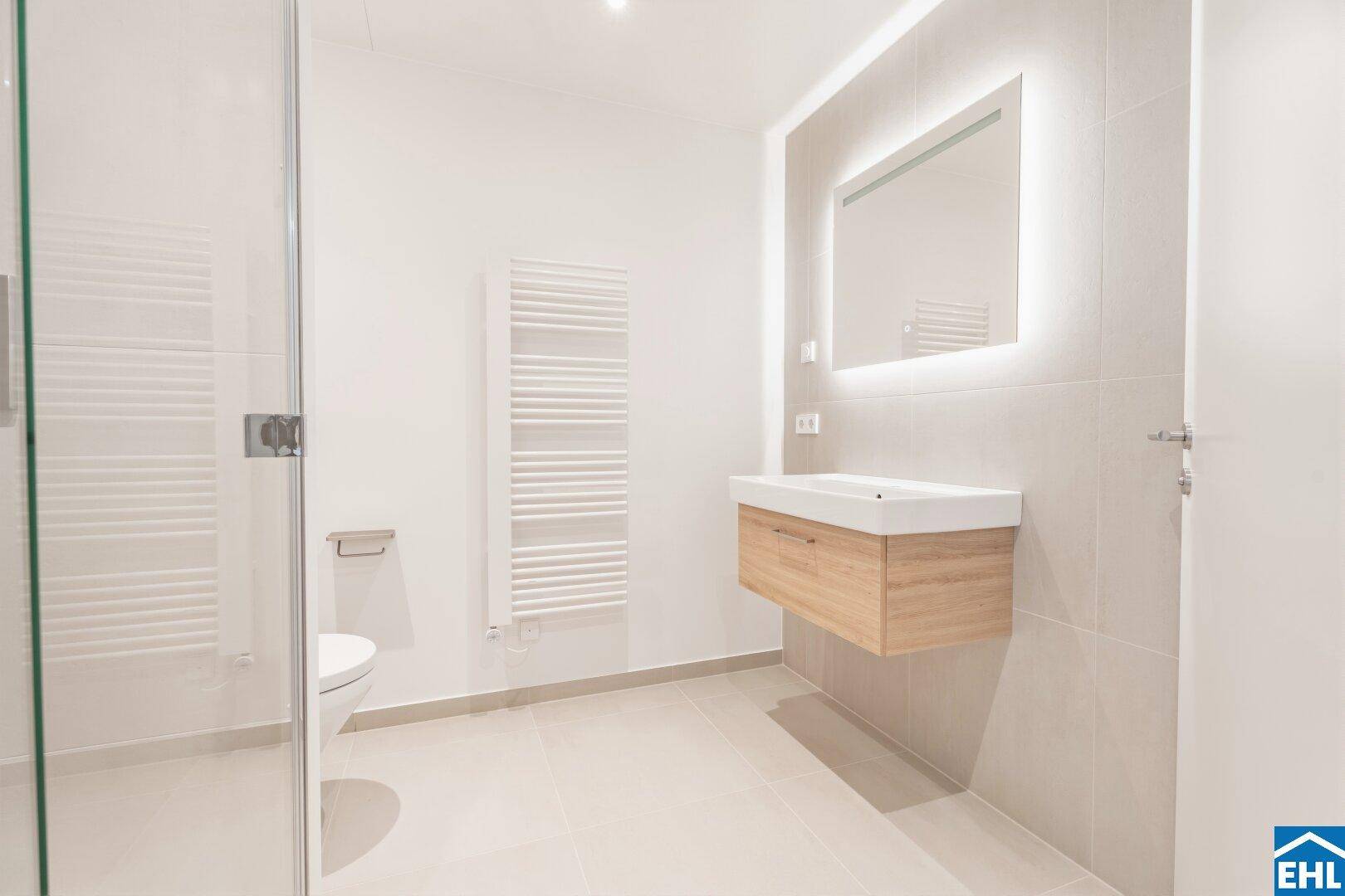 Modernes Badezimmer mit begehbarer Dusche, schwebendem Waschtisch und beleuchtetem Spiegel.