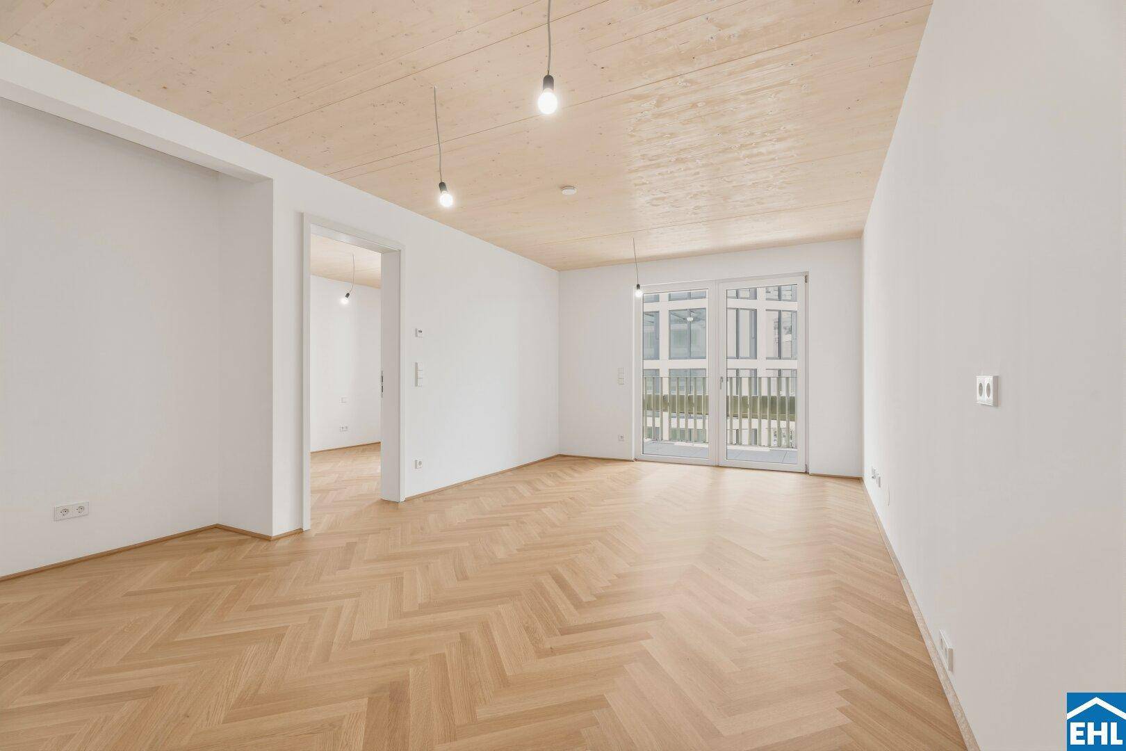Geräumiger, heller Wohnraum mit Fischgrätparkett und Holzdecke, bietet direkten Zugang zum Außenbereich.