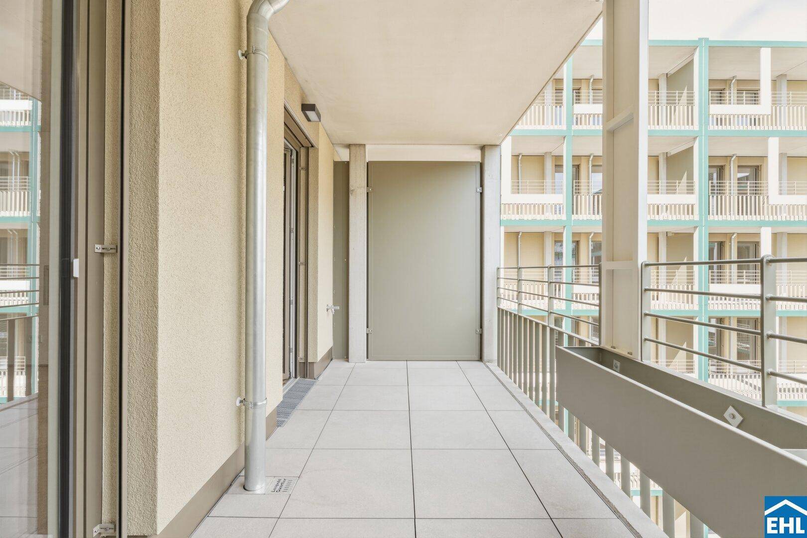 Langer Balkon mit Fliesenboden und Blick auf die moderne Architektur des Innenhofs.