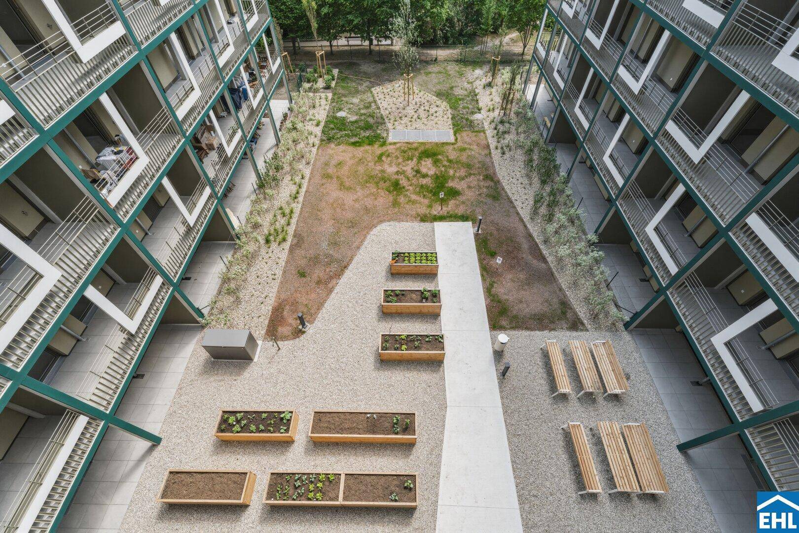 Grüner Innenhof mit Hochbeeten und Sitzgelegenheiten, umgeben von modernen Wohngebäuden.