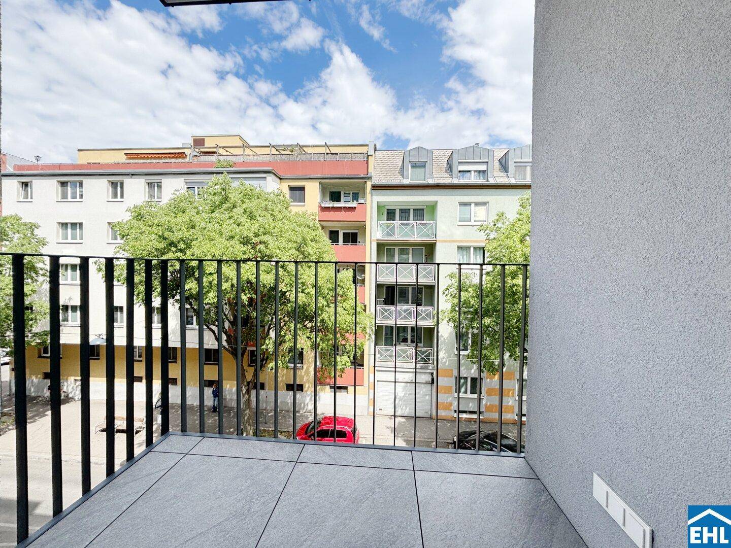 Balkon mit Fliesenboden und Blick auf die umliegenden Gebäude und Bäume der Stadt.