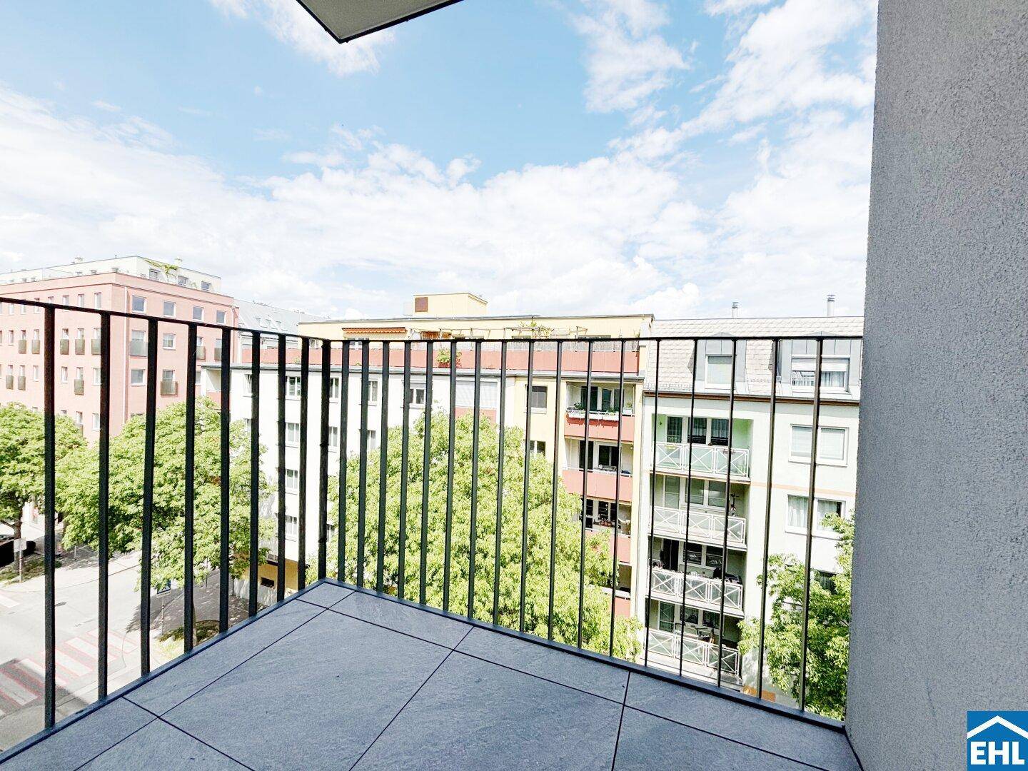 Balkon mit Fliesenboden und Metallgeländer, bietet einen Blick auf die umliegenden Gebäude und Bäume.