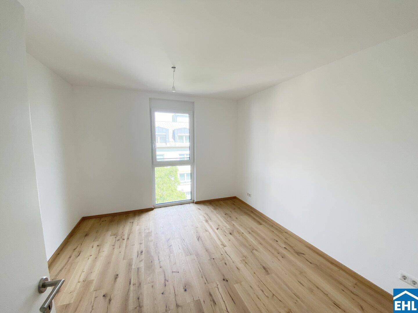 Helles Schlafzimmer mit Holzboden und großem Fenster, bereit zum Einrichten.