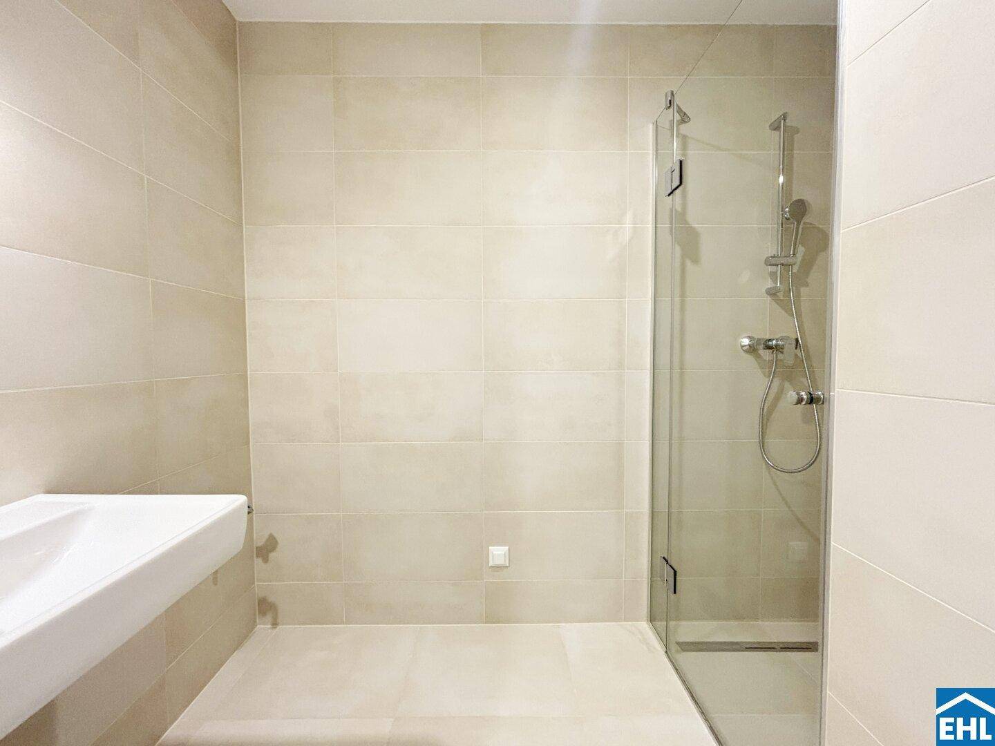 Modernes Badezimmer mit beigefarbenen Fliesen, ebenerdiger Dusche und schwebendem Waschbecken.