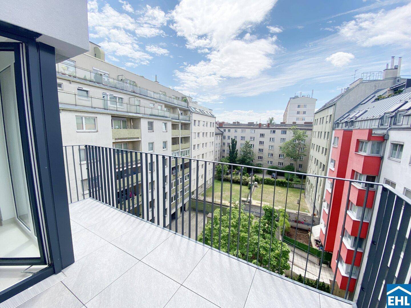 Geräumiger Balkon mit Fliesenboden und Blick auf den grünen Innenhof und umliegende Gebäude.