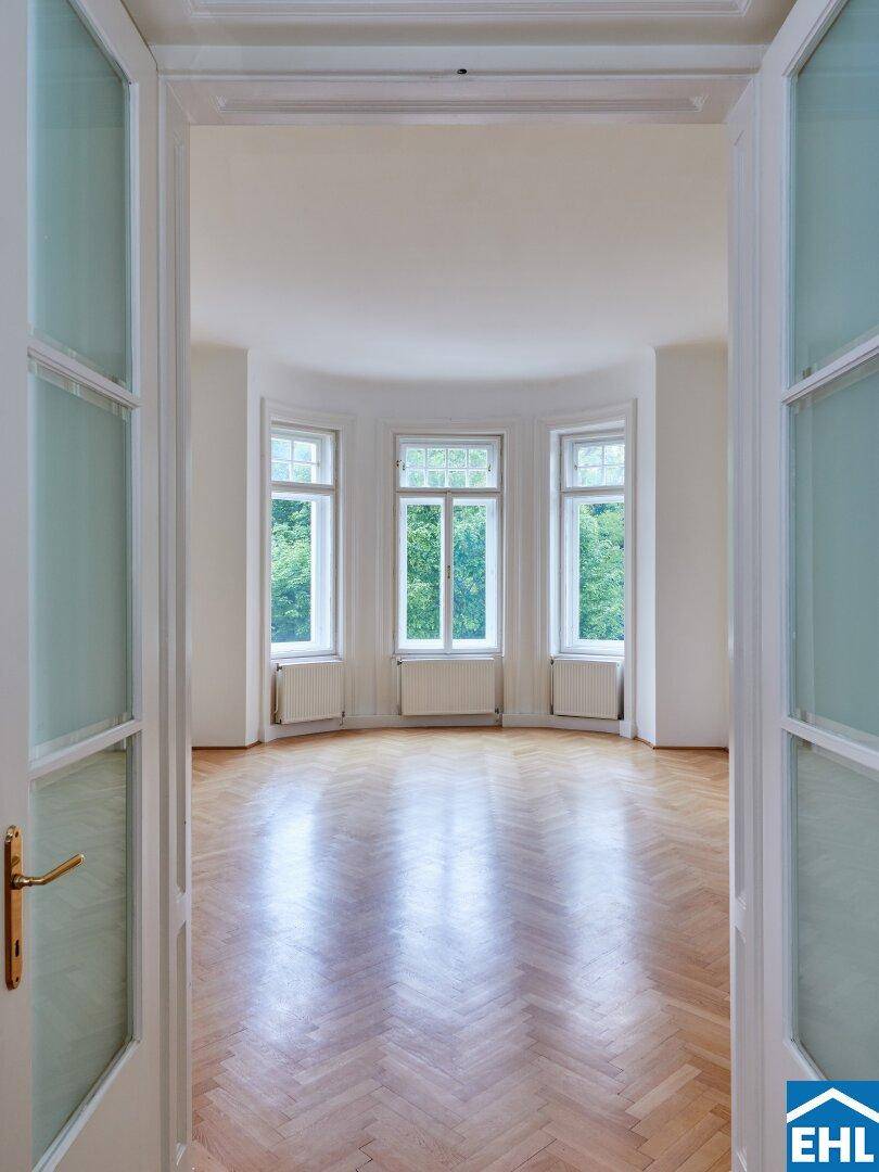 Helles Wohnzimmer mit Fischgrätparkett und großen Fenstern mit Blick ins Grüne.