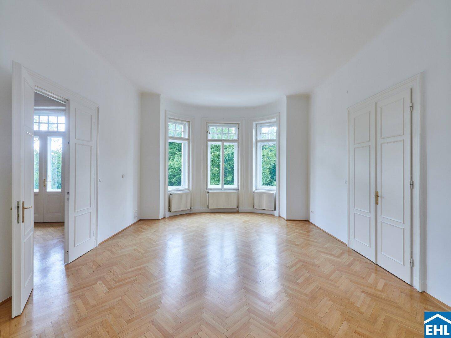 Geräumiges Wohnzimmer mit klassischem Fischgrätparkett und vielen Fenstern.