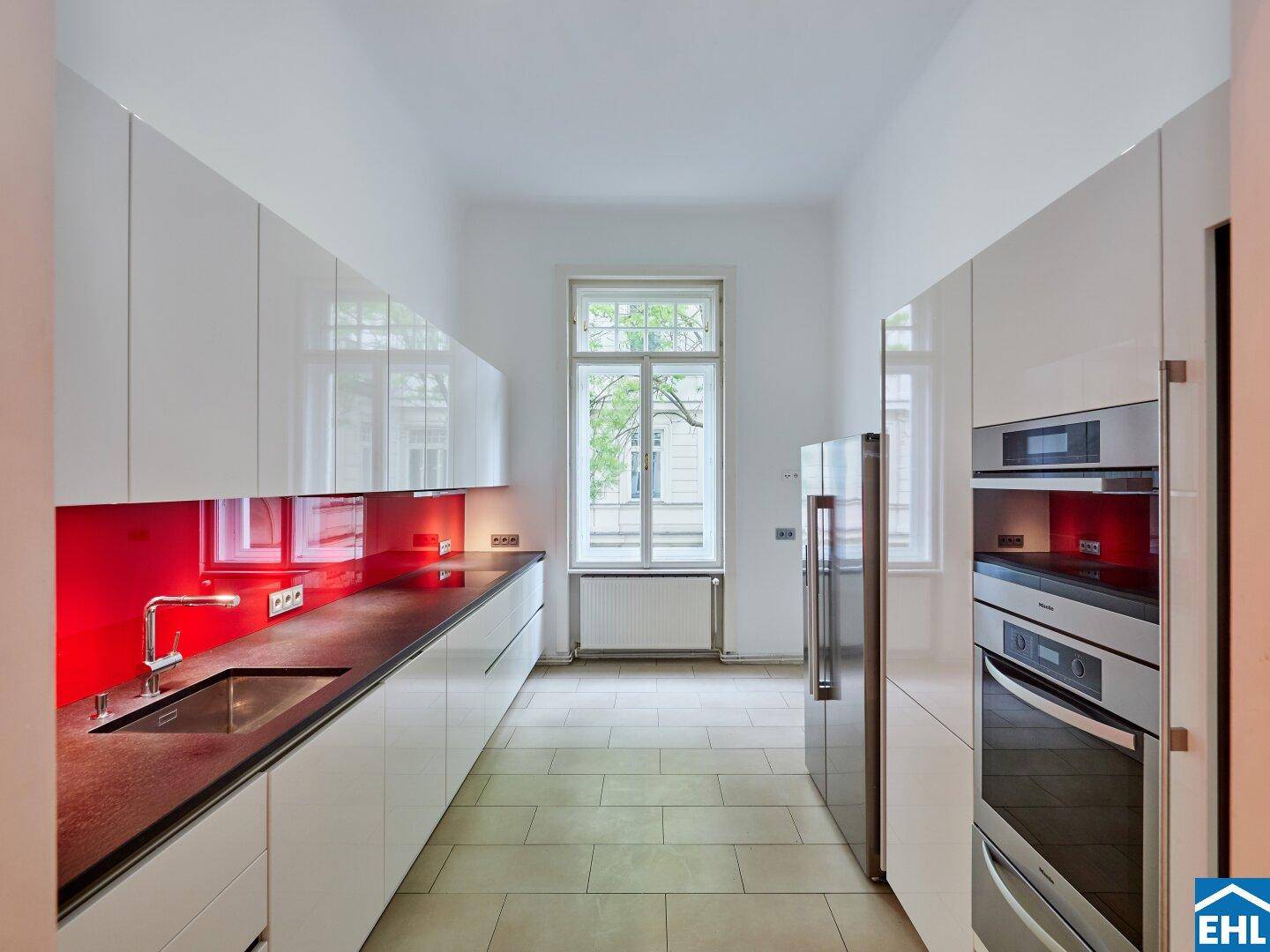 Moderne Küche mit weißen Hochglanzfronten, roter Rückwand und integrierten Geräten.