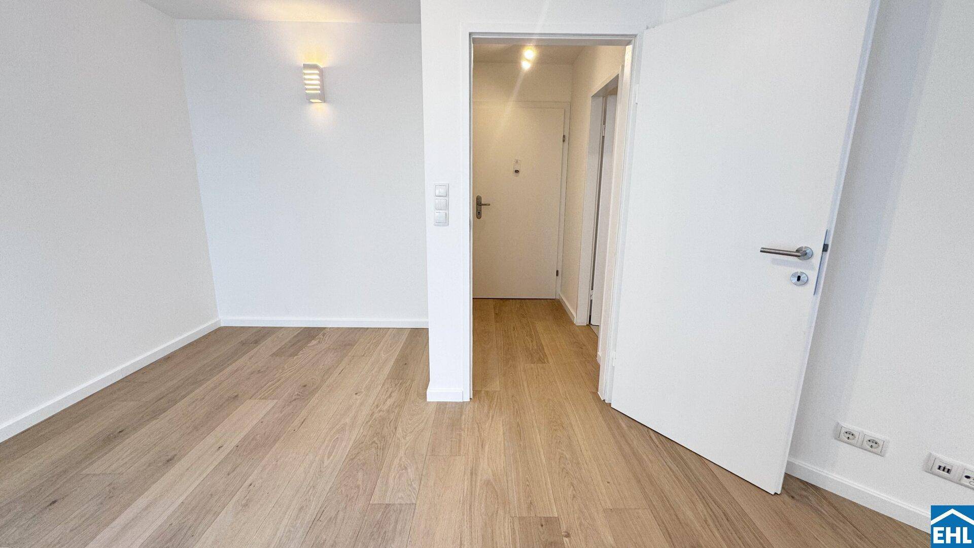 Heller Flur mit Holzboden und weiß gestrichenen Wänden, der zu weiteren Räumen führt.
