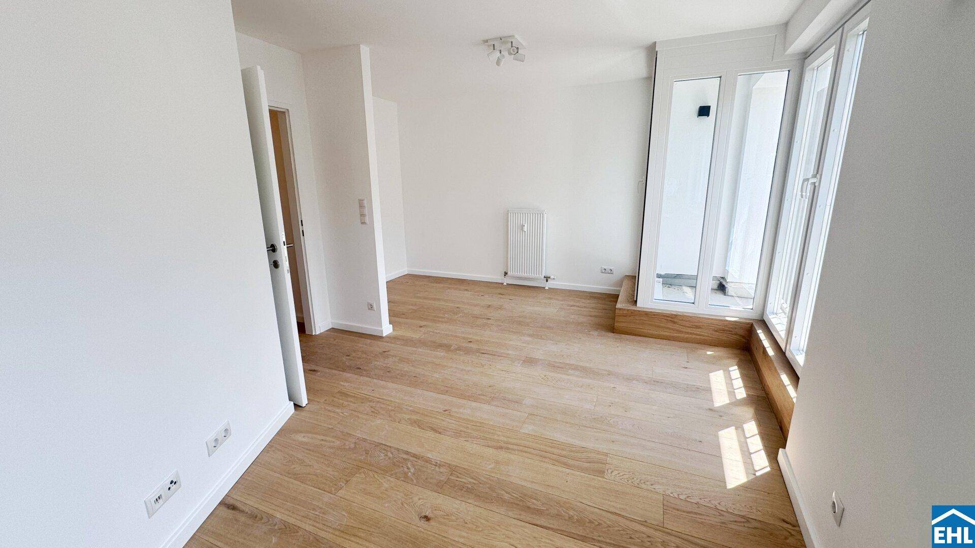 Helles, leeres Zimmer mit Holzboden, weißen Wänden und Zugang zu einem französischen Balkon.