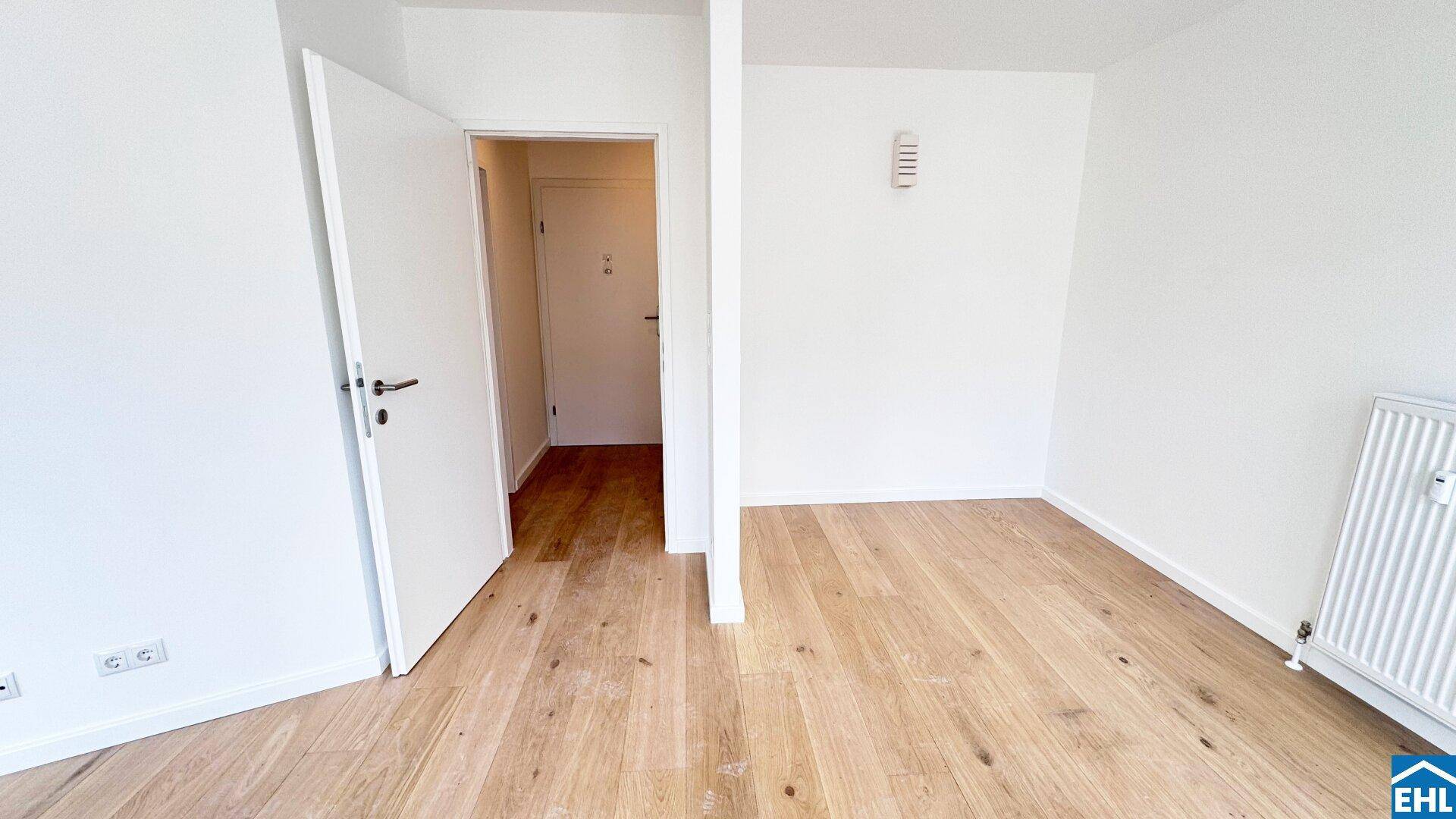 Leerer Raum mit Holzboden, weißen Wänden und einem Heizkörper, der auf eine allgemeine Nutzung hindeutet.