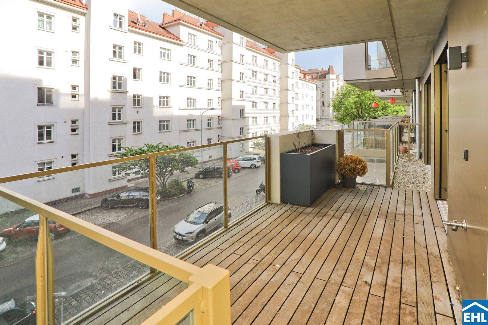 Heller Balkon mit Holzdeck und Glasgeländer, bietet einen Blick auf die umliegende Stadtlandschaft.