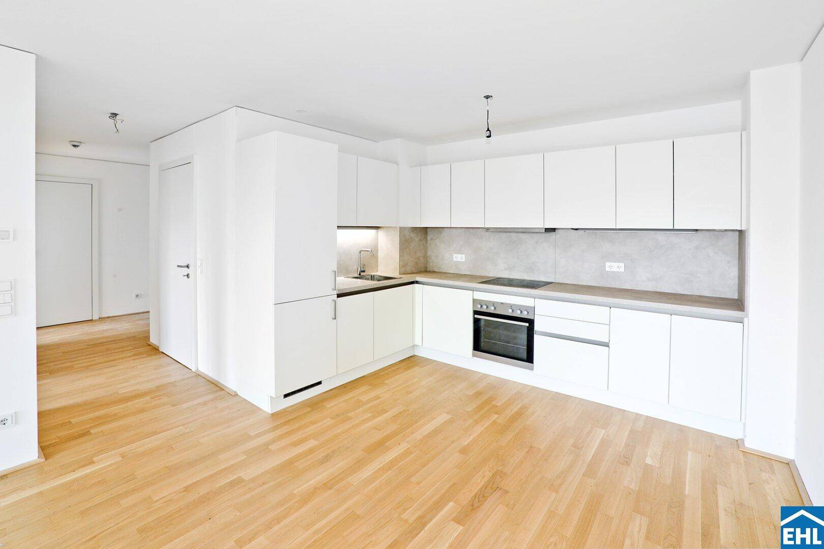Moderne, helle Küche mit weißen Schränken, integrierten Geräten und Parkettboden.