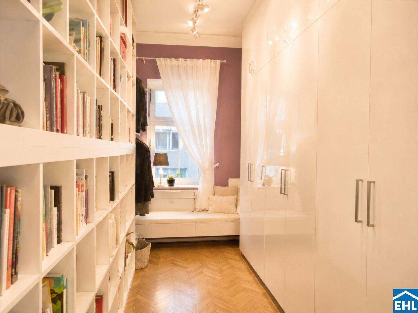 Langer Flur mit maßgefertigten weißen Einbauschränken, Bücherregalen und einer gemütlichen Fenstersitzbank.