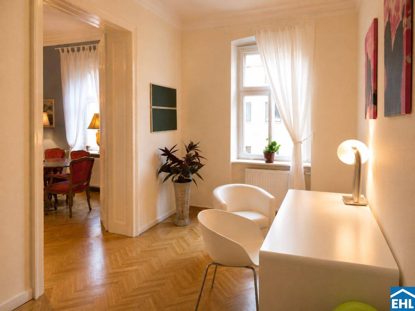 Heller Arbeitsbereich mit Schreibtisch und Stühlen, der einen Blick in den angrenzenden Essbereich bietet.
