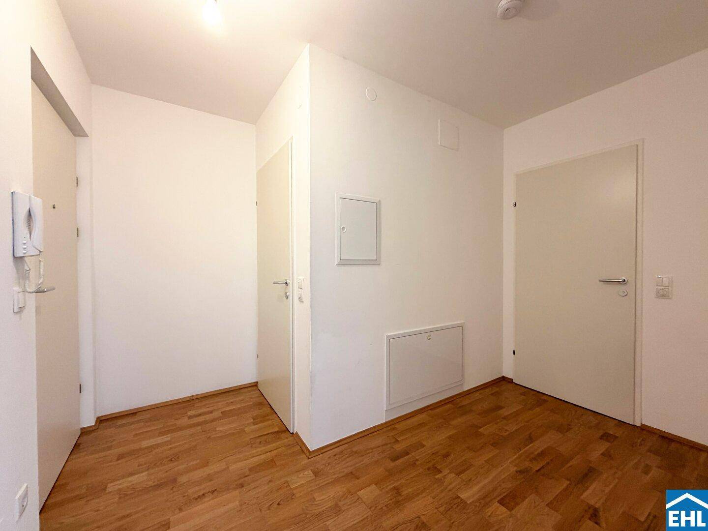Heller Flur mit Parkettboden, weißen Türen und Gegensprechanlage.
