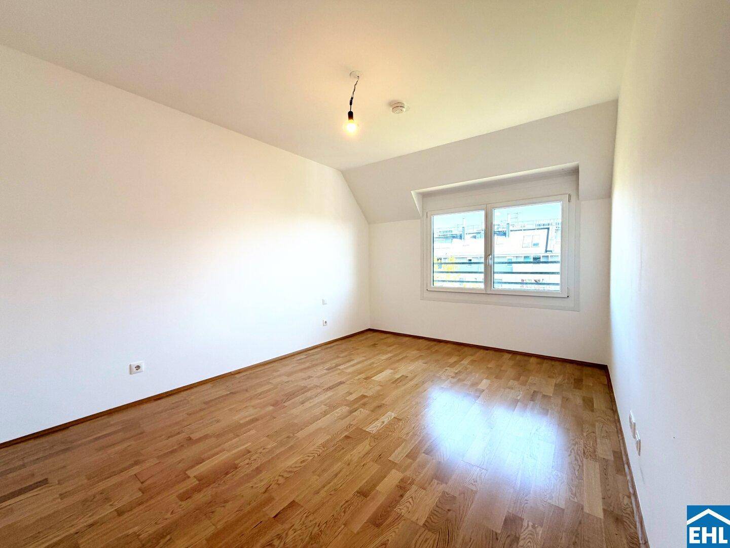 Helles Schlafzimmer mit Parkettboden, großem Fenster und Dachschräge.