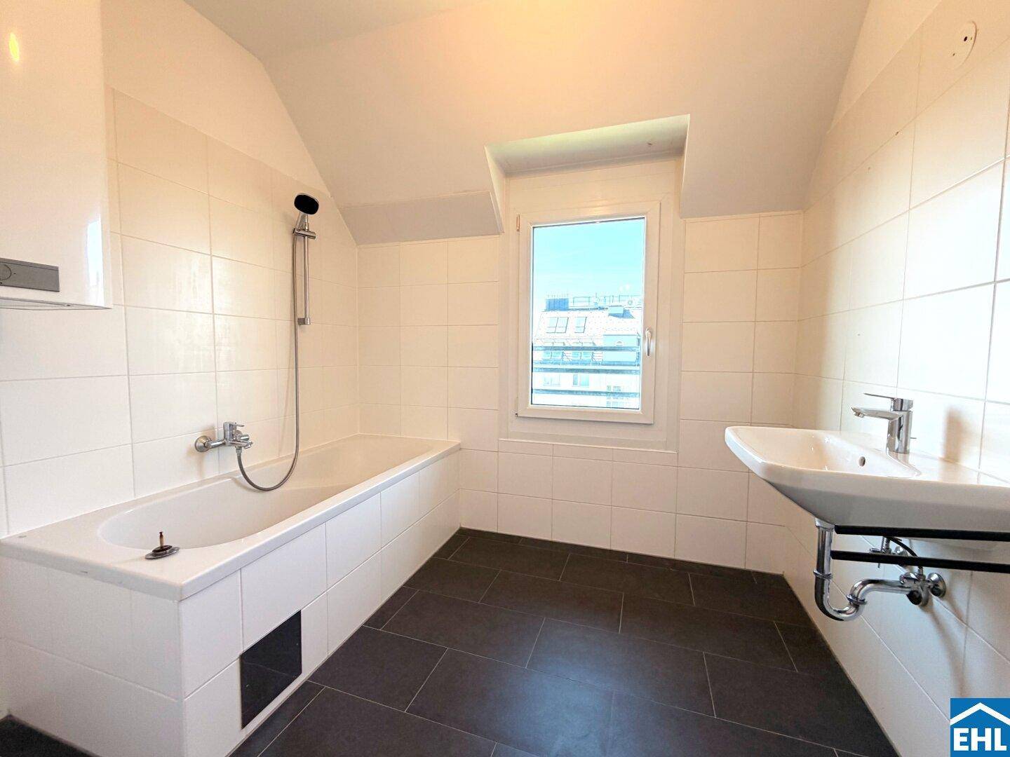 Gefliestes Badezimmer mit Badewanne, Waschbecken, Fenster und Dachschräge.