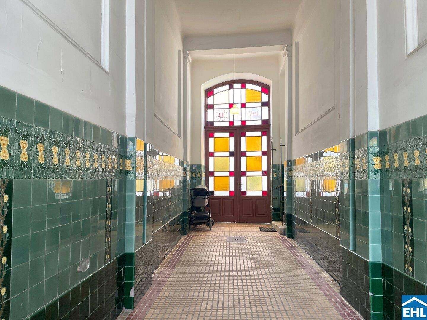 Historischer Eingangsbereich mit farbenfroher Bleiglas-Tür und dekorativen grünen Wandfliesen im Altbau.