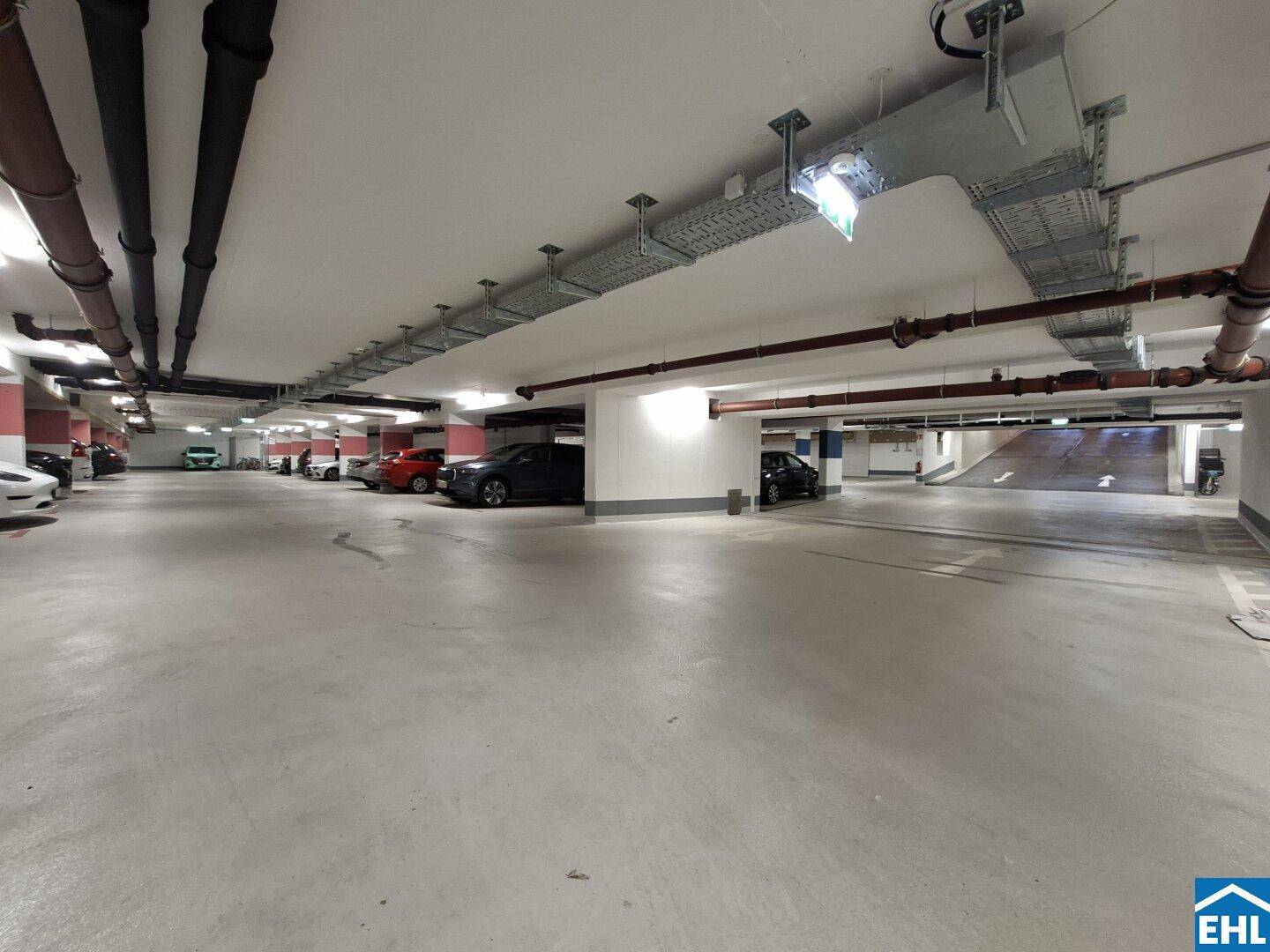 Weitläufige Tiefgarage mit zahlreichen Stellplätzen, moderner Beleuchtung und sichtbarer Gebäudetechnik.