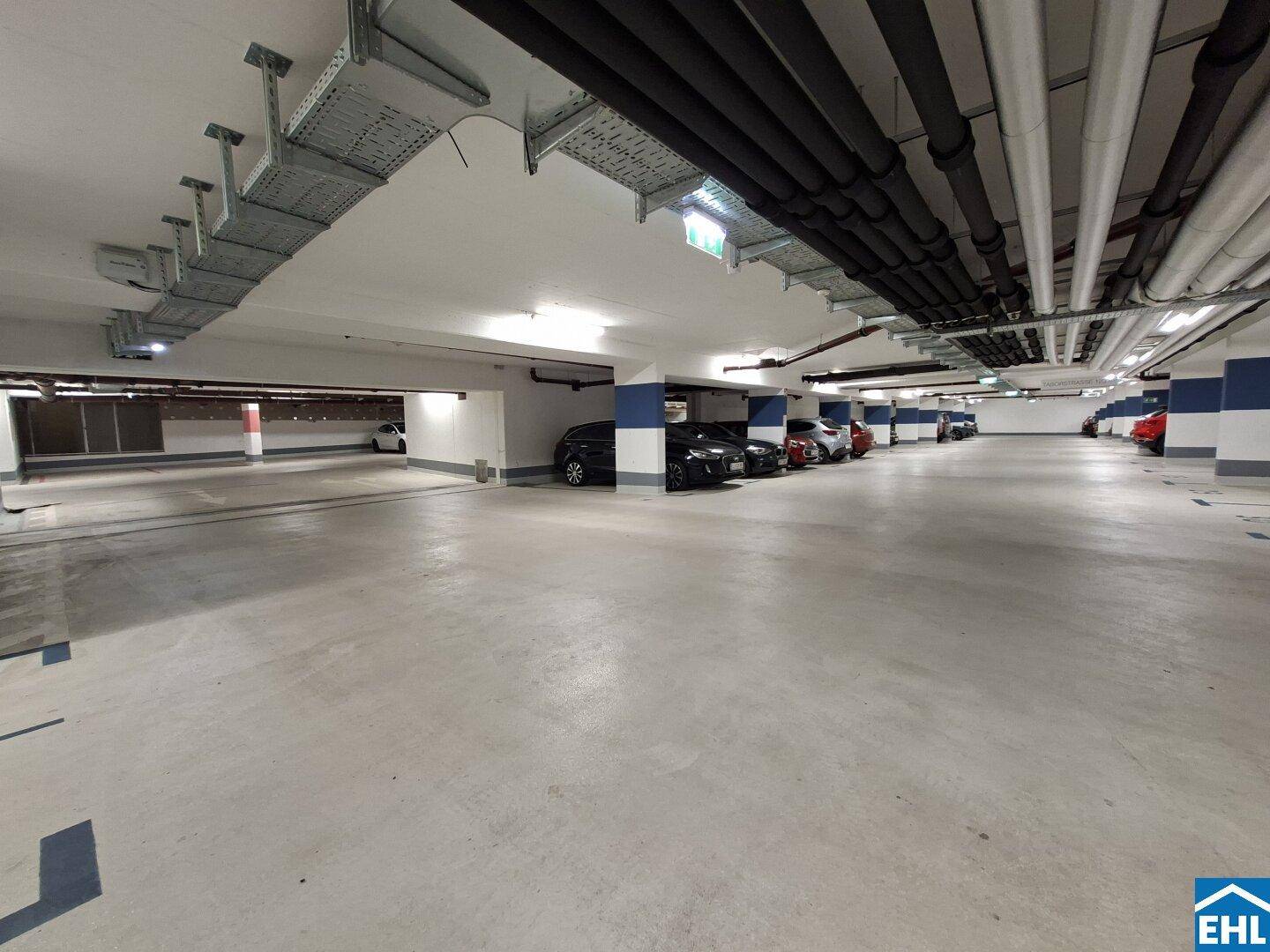Helle Tiefgarage mit markierten Stellplätzen, blauen Säulen und ordentlich geparkten Fahrzeugen.