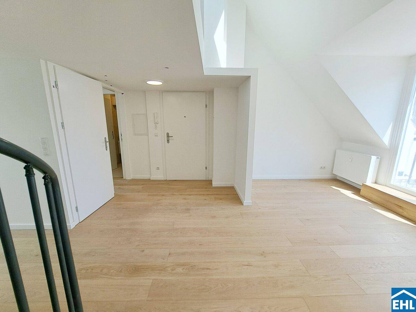 Heller Innenraum mit Holzfußboden, weißen Wänden und Zugangstür, teilweise mit Dachschräge.