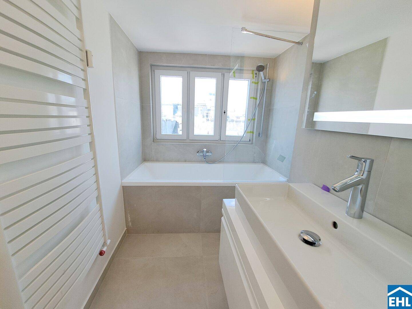 Modernes Badezimmer mit Badewanne, Einzelwaschbecken, beheiztem Handtuchhalter und Fenster.