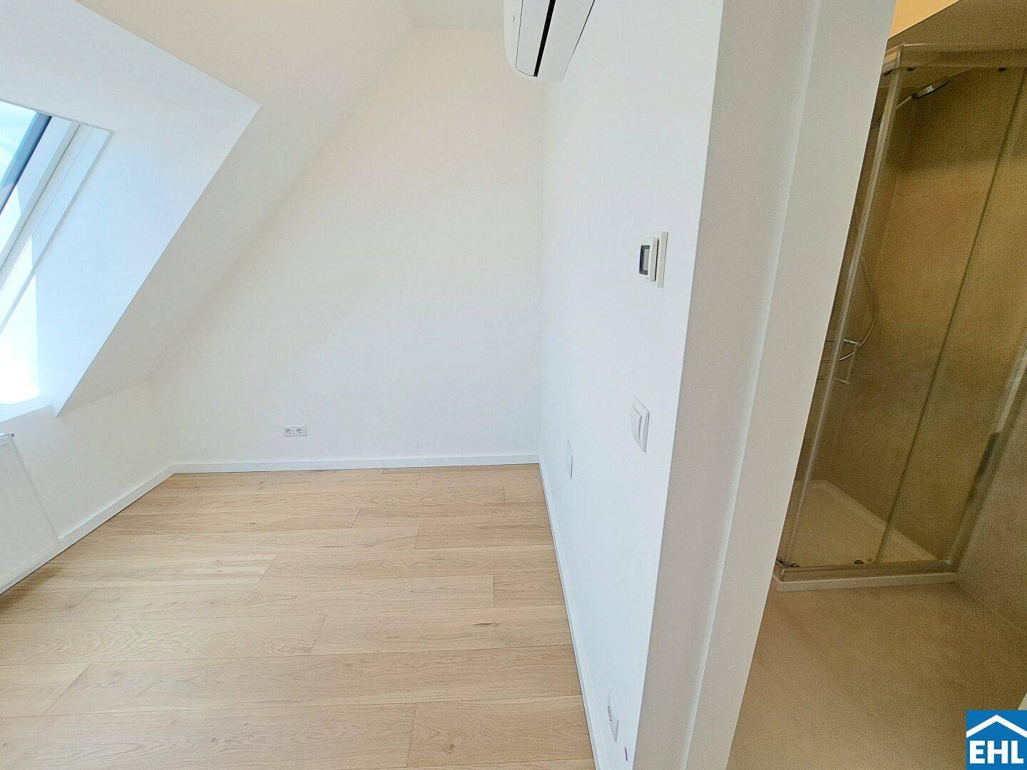 Helles Schlafzimmer mit Holzfußboden, Klimaanlage und angrenzendem Duschbereich.