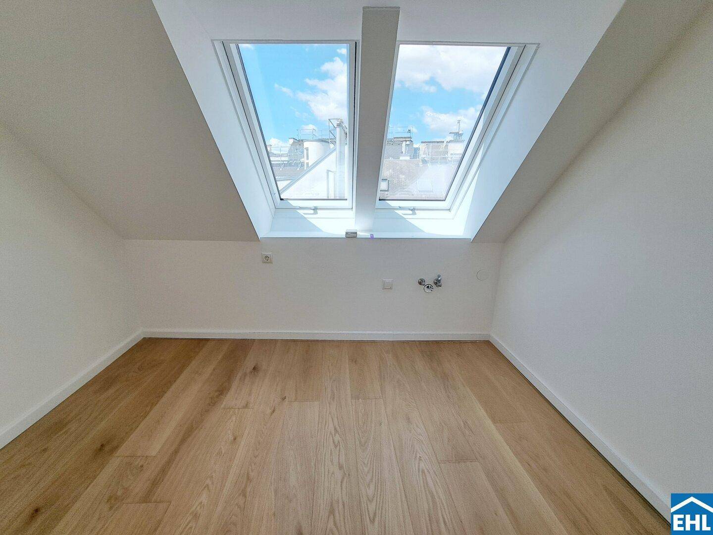 Heller Raum mit Holzfußboden und zwei großen Dachfenstern, die viel Tageslicht hereinlassen.