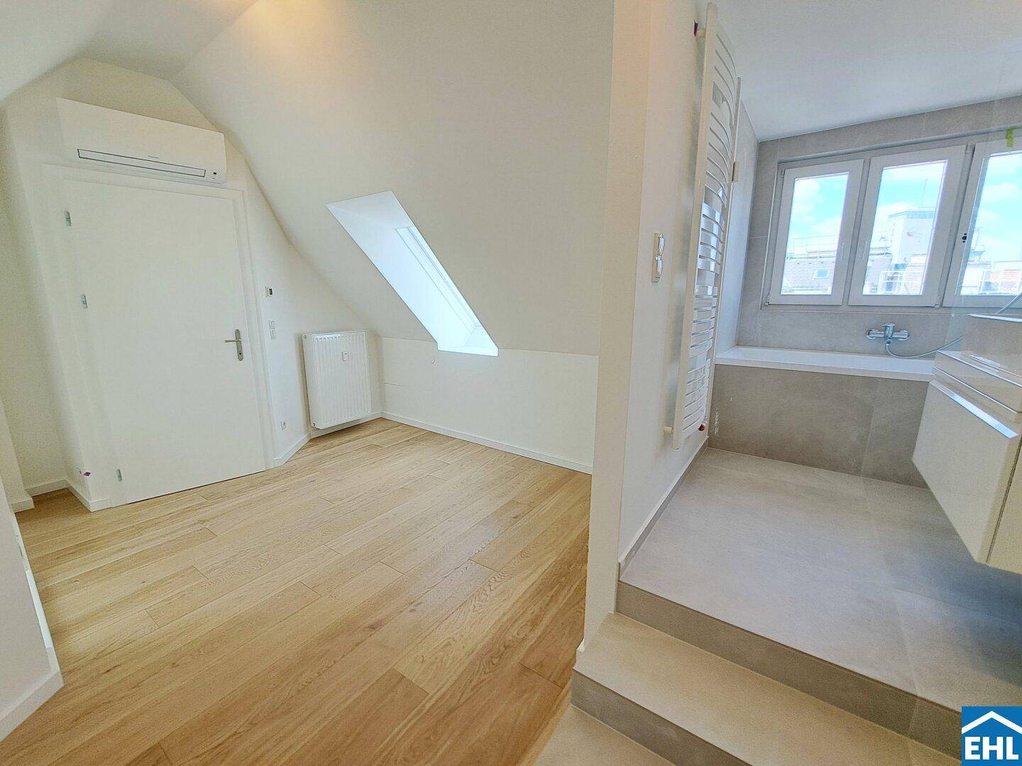 Helles Schlafzimmer mit Holzfußboden, Klimaanlage und direktem Zugang zum Badezimmer.